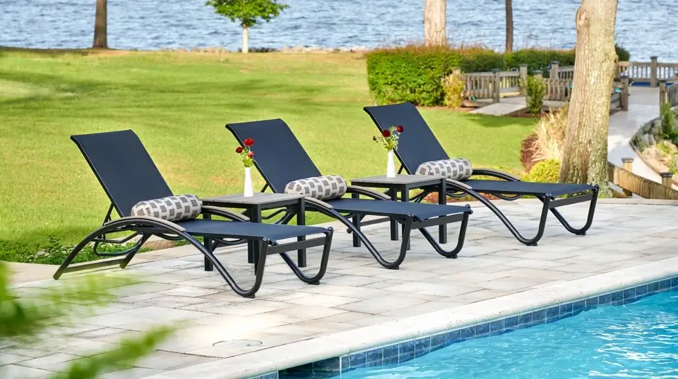 Commercial pool deck featuring Helios sling chaise lounges with side tables arranged beside a resort swimming pool for upscale guest relaxation.